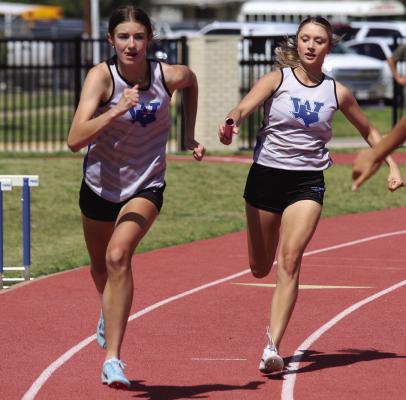 Trojanette sophomore Kenley Teakell takes the handoff from senior Isabel Bussey in the 4x100 relay at the Area track meet in Graham on Thursday, April 10. Photo/Landon Davis
