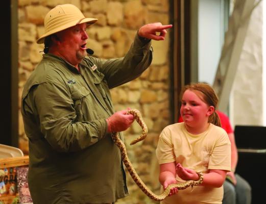 The Creature Teacher, Mr. B, shows off a rat snake with the help of an assistant at the Archer Public Summer Reading Program on Wednesday, June 17. Photo/Nathan Lawson