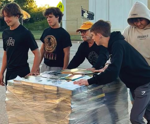 Members of the Archer City HS football team work with Johnny Bart Hudson to move part of Larry McMurtry’s book collection across South Center Street. Courtesy photo/Cynthia Getschow