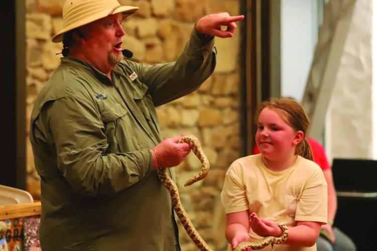 The Creature Teacher, Mr. B, shows off a rat snake with the help of an assistant at the Archer Public Summer Reading Program on Wednesday, June 17. Photo/Nathan Lawson